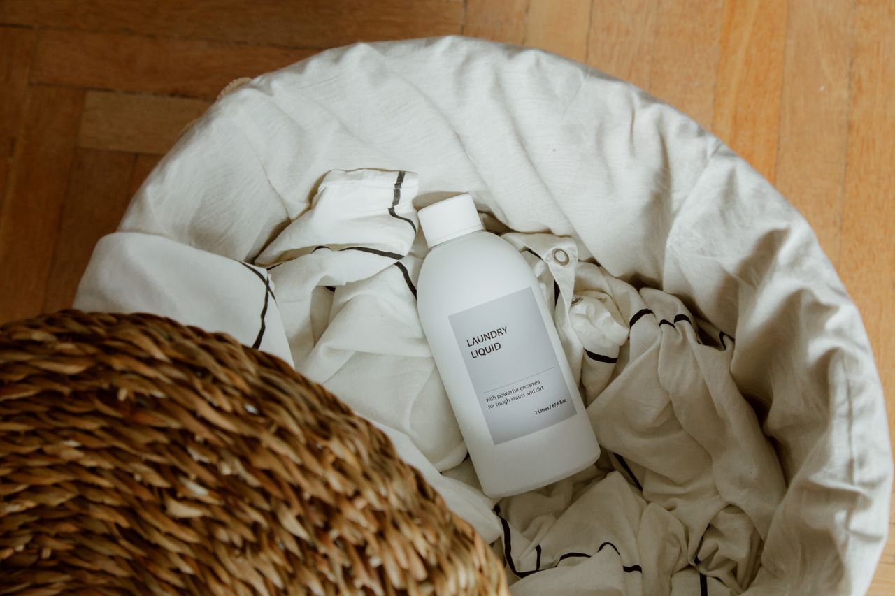 Services-03 High angle view of laundry liquid in basket with white linens on wooden floor.