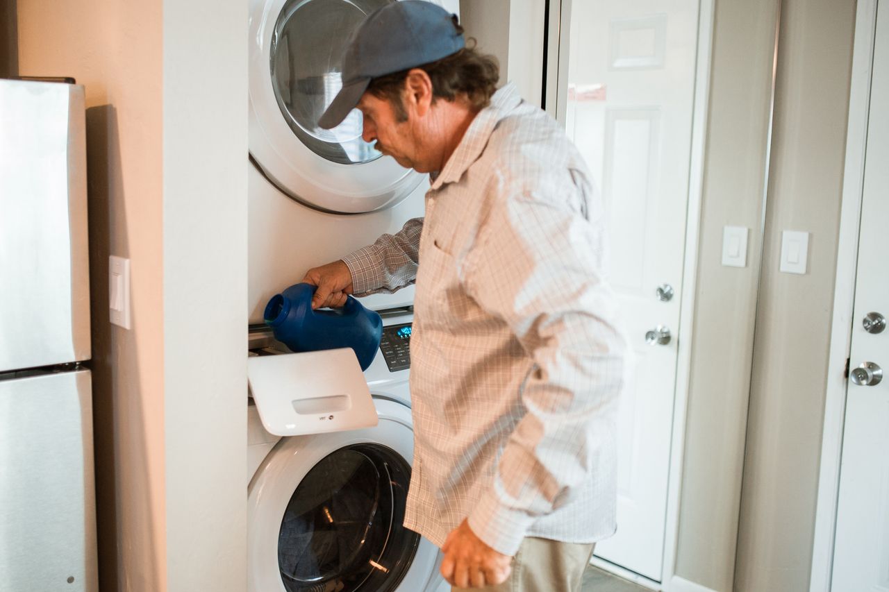 why-choose-us Man pouring liquid detergent into a stacked washer and dryer in a modern laundry room.